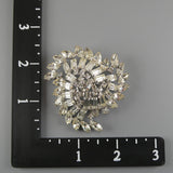Silver brooch on a gray background with a ruler for scale