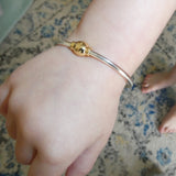 Close-up of a wrist wearing a gold and silver bracelet on a patterned carpet.